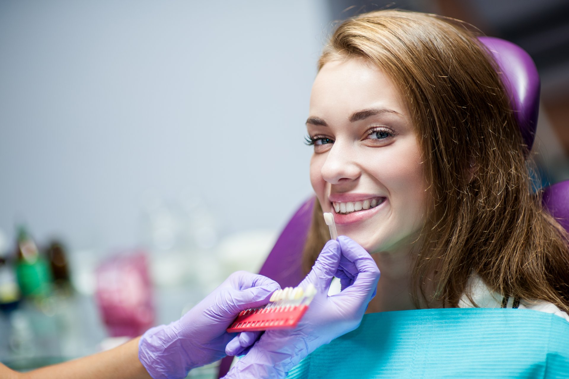 Chica sonríe mientras la dentista compara piezas dentales para un implante